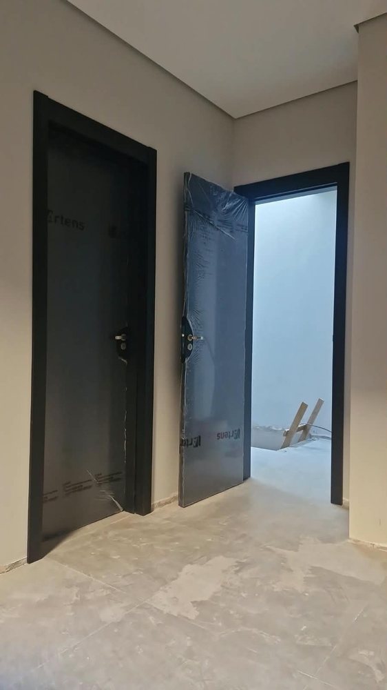 Porta preta com batente preto e ferragem, instalada durante obra, ao lado de vão sem porta
